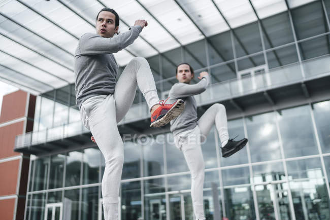 Jovens gêmeos do sexo masculino treinando com joelhos levantados — Fotografia de Stock
