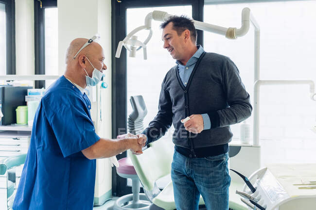 Dentist and male patient in dentist office, shaking hands — Stock Photo