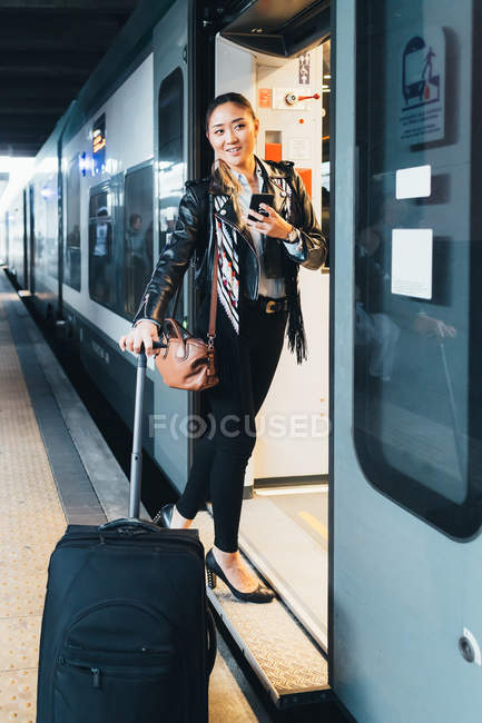 Женщина с чемоданом на колесах садится в поезд — стоковое фото