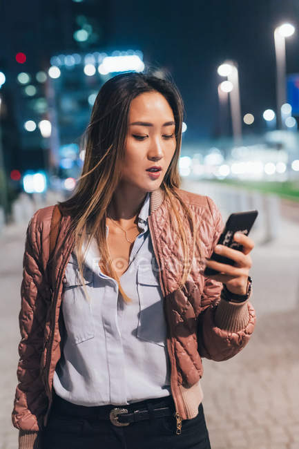 Woman standing outdoors at night and using smartphone — Stock Photo