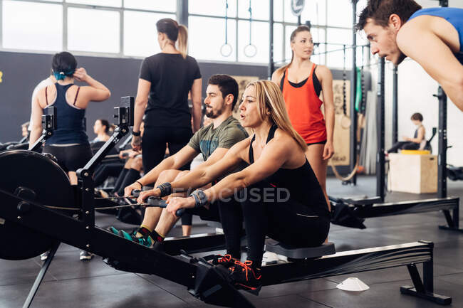 Les gens qui utilisent des rameurs dans la salle de gym — Photo de stock
