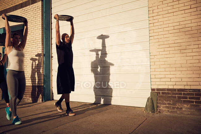 People with arms raised carrying weights equipment — Stock Photo
