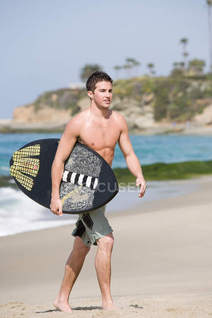 Young man carrying surfboard on beach — Stock Photo