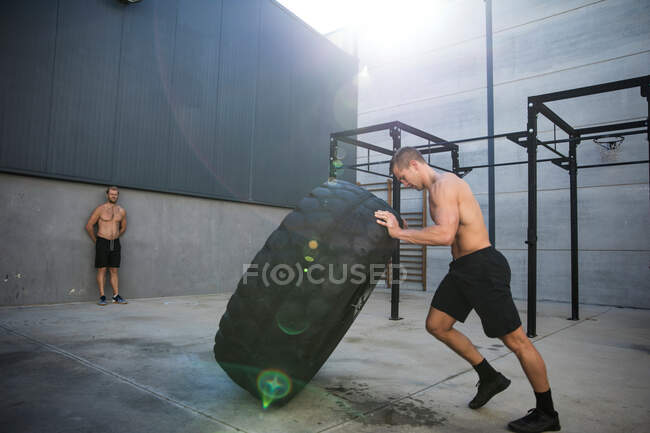 Uomo che si allena in palestra, sollevando pneumatici — Foto stock