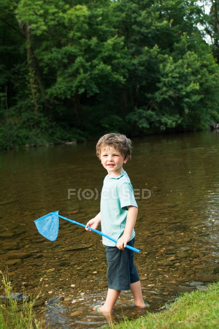 Niño sosteniendo red de pesca por río - foto de stock