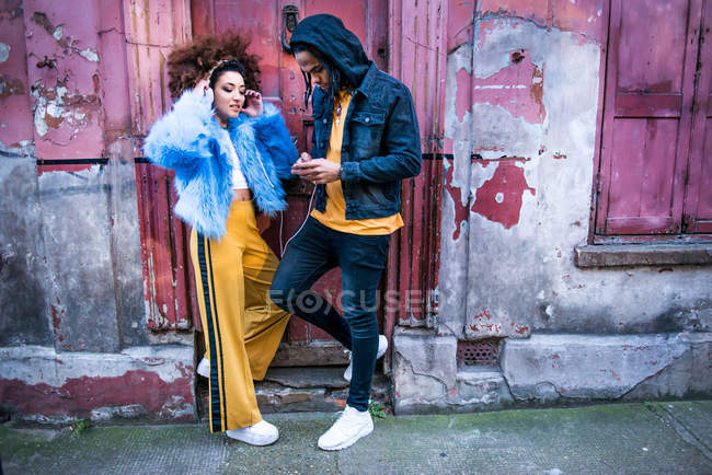 Молодая пара на улице слушает музыку через наушники на смартфоне — стоковое фото