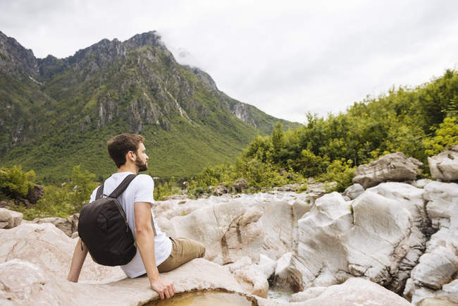 Hombre sentado en las rocas y mirando a las montañas Malditas, Theth, Shkoder, Albania, Europa - foto de stock