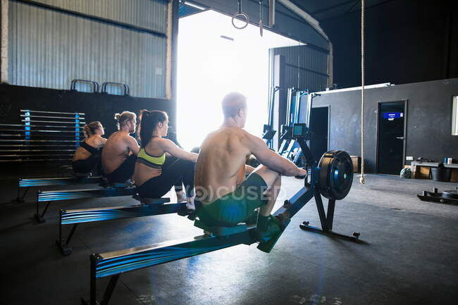 Gruppe von Menschen, die in der Sporthalle trainieren, mit Rudergeräten, Rückansicht — Stockfoto