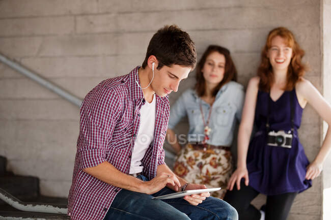 Hombre joven usando una tableta digital con mujeres jóvenes en el fondo - foto de stock