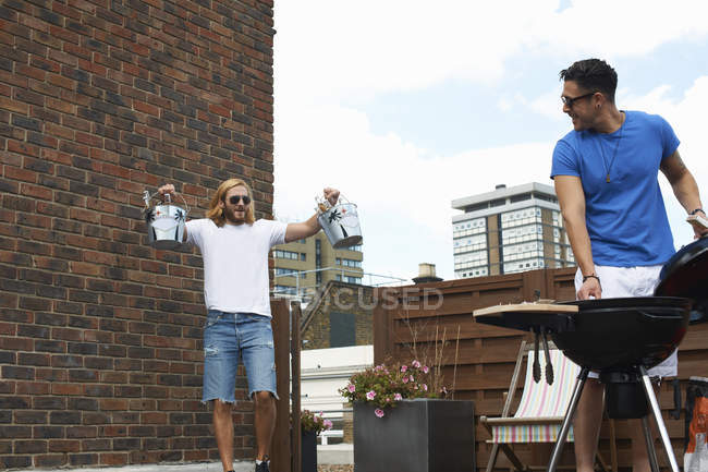 Young man carrying ice buckets at rooftop barbecue — Stock Photo