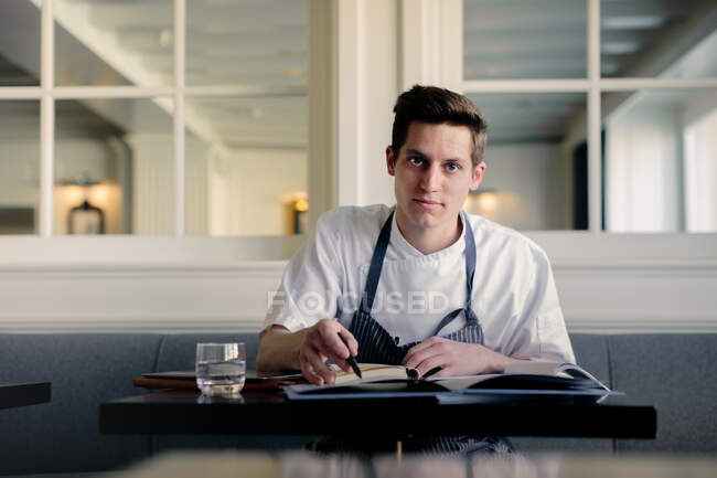 Chef joven haciendo papeleo y hablando en smartphone en restaurante - foto de stock