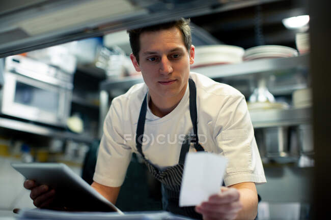 Joven chef masculino usando tableta digital y leyendo el orden de los alimentos en la cocina - foto de stock