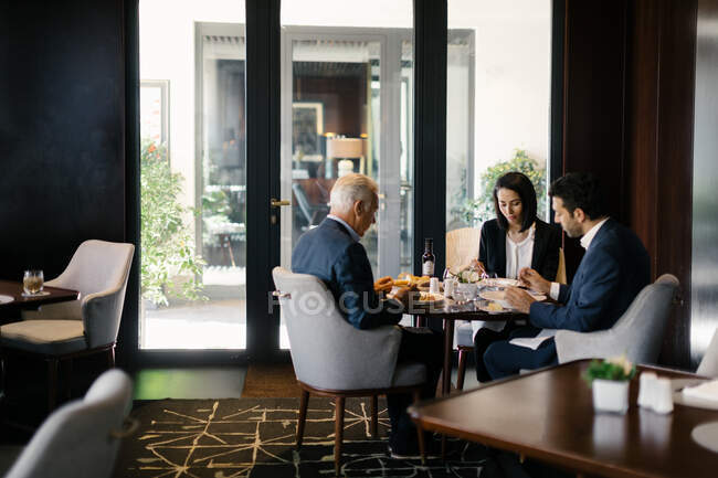 Two businessmen and woman having working lunch in hotel restaurant — Stock Photo