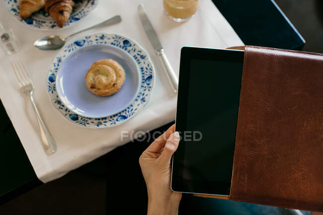 La mano de la mujer que quita la tableta digital de la caja mientras desayuna en el hotel boutique en Italia - foto de stock