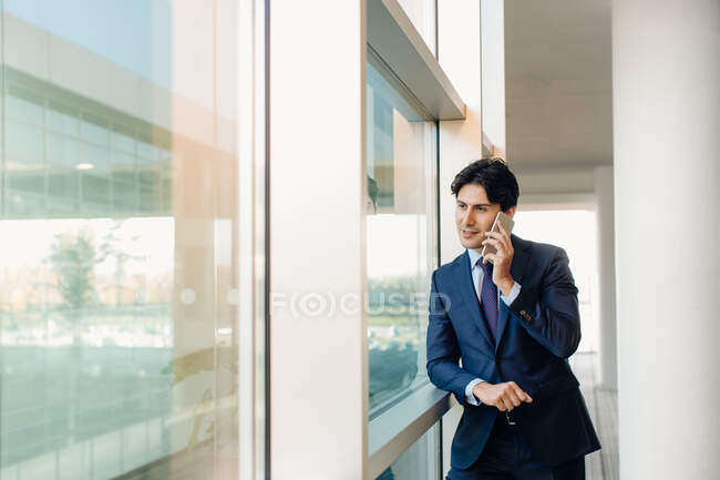 Бизнесмен, использующий мобильный телефон по окнам — стоковое фото
