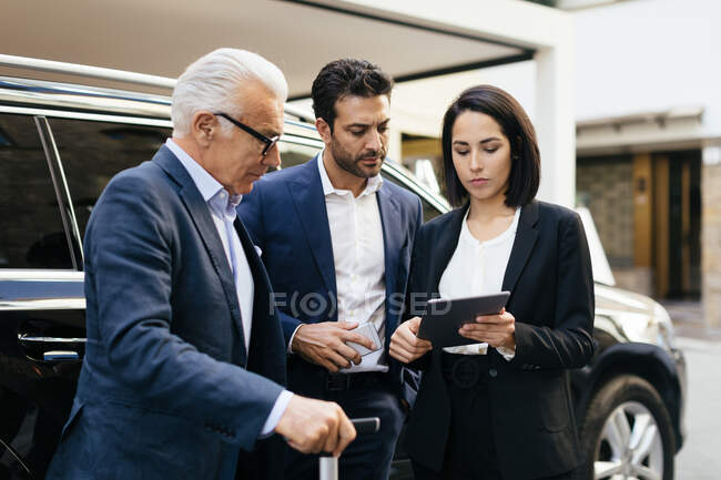 Dos hombres de negocios y una mujer fuera del hotel mirando la tableta digital - foto de stock