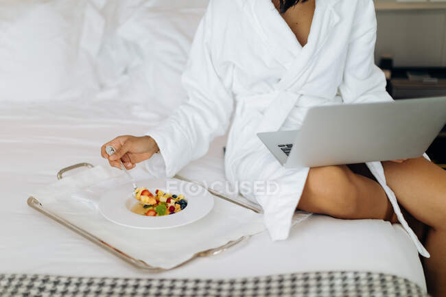 Femme utilisant un ordinateur portable et prenant le petit déjeuner en suite — Photo de stock