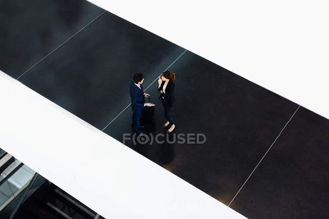 Businessman and businesswoman with wheeled luggage in hotel building — Stock Photo