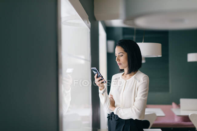 Young businesswoman in hotel looking at smartphone — Stock Photo