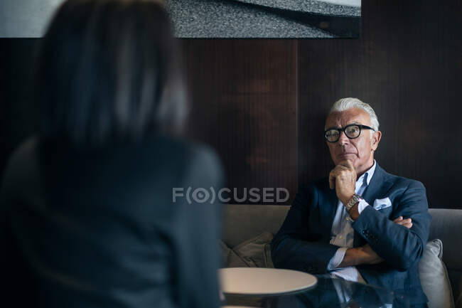 Homme d'affaires senior assis à la table de l'hôtel réunion avec une femme d'affaires, vue sur l'épaule — Photo de stock