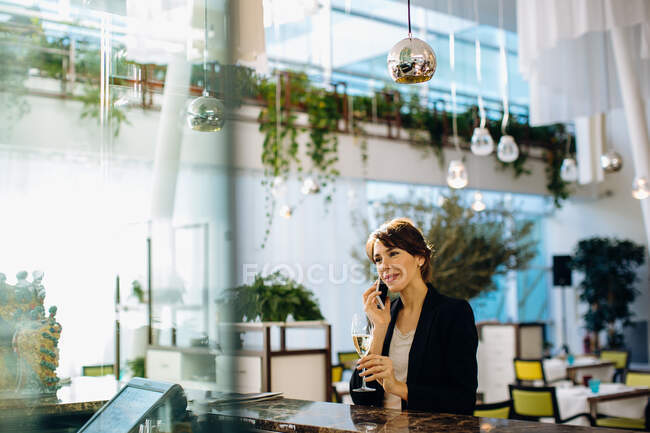 Femme d'affaires utilisant un téléphone portable tout en buvant un verre au bar — Photo de stock