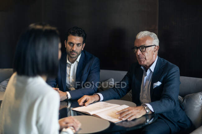 Dos hombres de negocios sentados en la mesa del hotel reuniéndose con una mujer de negocios - foto de stock