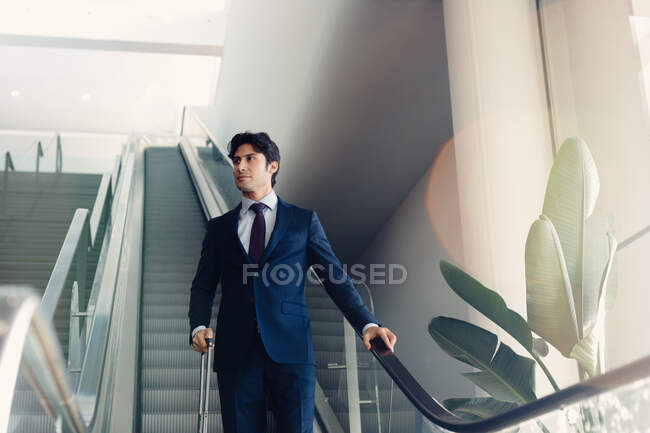 Homme d'affaires avec bagages à roues sur l'escalier roulant de l'hôtel — Photo de stock
