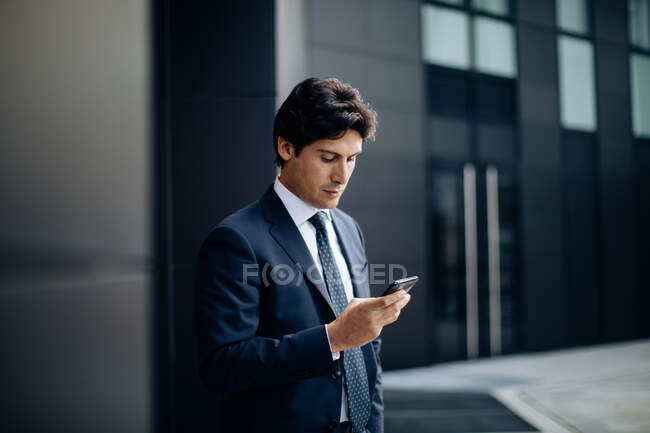 Businessman using smartphone in front of office building — Stock Photo