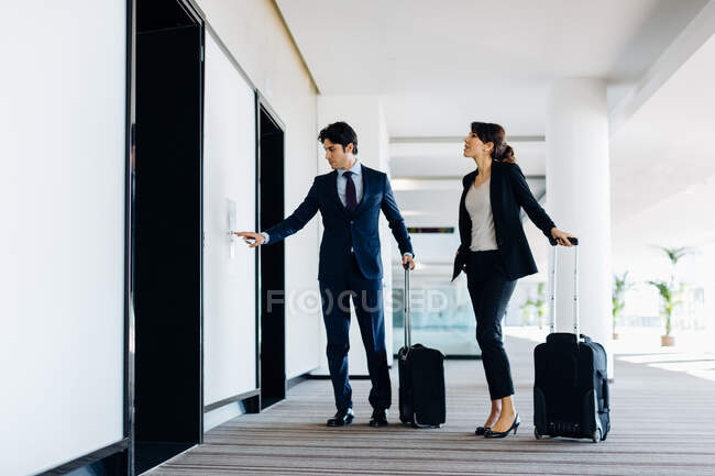 Businessman and businesswoman with wheeled luggage waiting for hotel escalators — Stock Photo