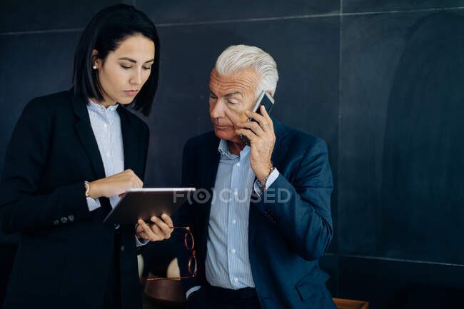Empresario y mujer mirando la tableta digital y haciendo una llamada de teléfono inteligente en la sala de juntas - foto de stock