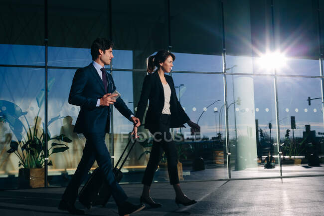 Businessman and businesswoman with wheeled luggage passing glass building, Malpensa, Milan — Stock Photo