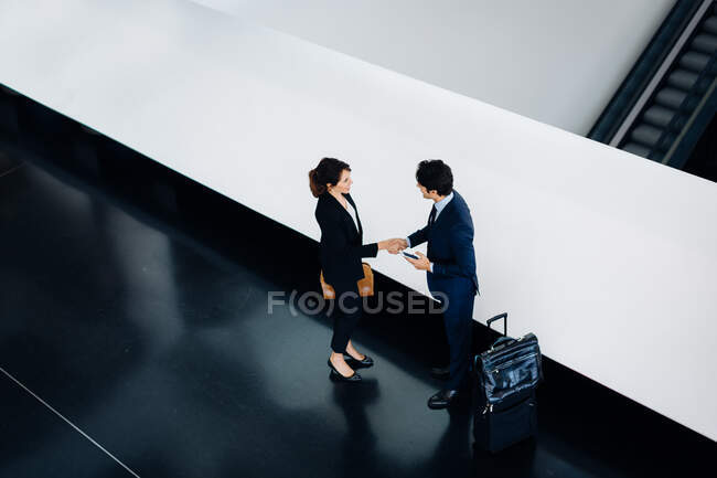 Businessman and businesswoman with wheeled luggage in hotel building — Stock Photo