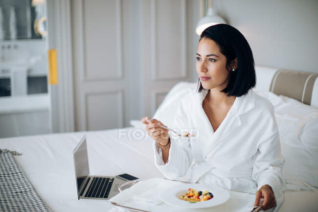 Woman using laptop and having breakfast in suite — Stock Photo