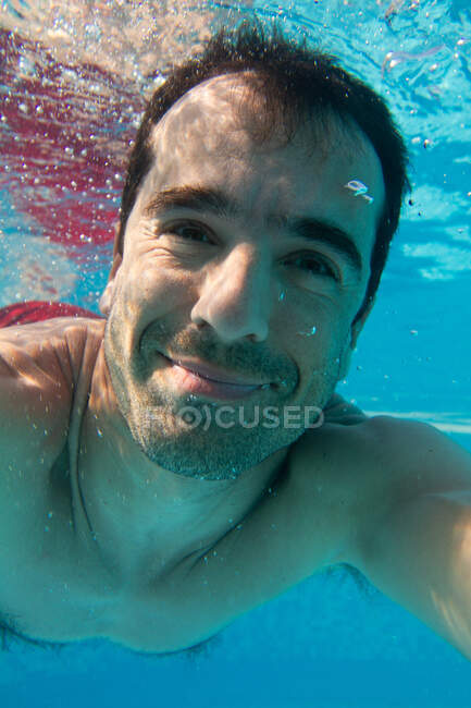 Un hombre nadando bajo el agua, sonriendo a una cámara, un selfie bajo el agua. - foto de stock