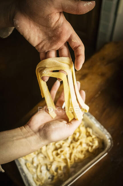 High angle close up of person placing freshly made Tagliatelle pasta in a metal tray. — Stock Photo