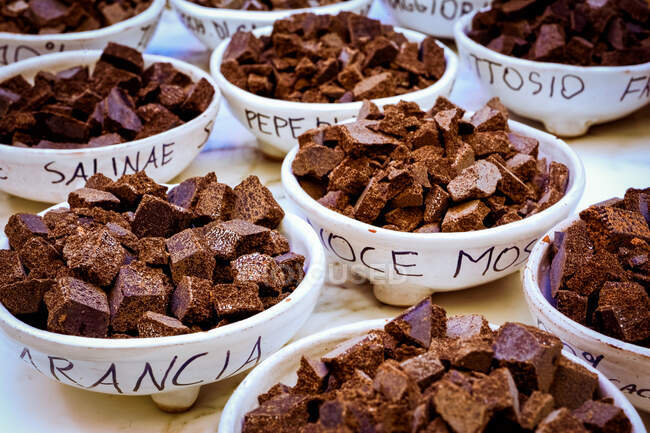High angle close up of different types of chocolates in white ceramic bowls with black handwriting in Modica, Sicily, Italy. — Stock Photo