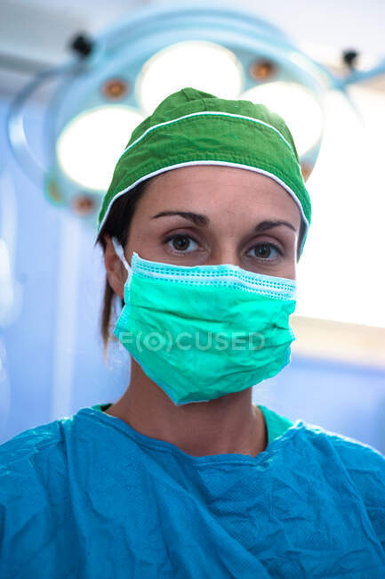 Retrato de cabeza y hombros de una cirujana vestida con exfoliantes y máscara quirúrgica, mirando a la cámara. - foto de stock