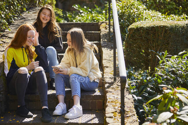 Три девочки сидят на улице на лестнице, проверяют мобильный телефон. — стоковое фото
