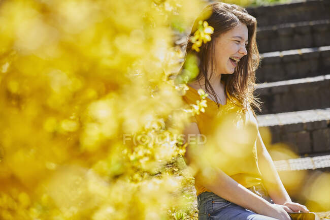 Adolescente sentada ao ar livre em degraus, Forsythia amarelo em primeiro plano. — Fotografia de Stock