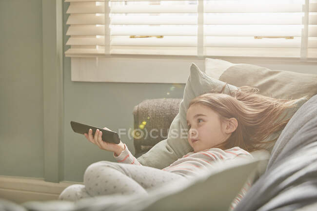 Mädchen liegt im Schlafanzug auf einem Sofa und schaut fern. — Stockfoto