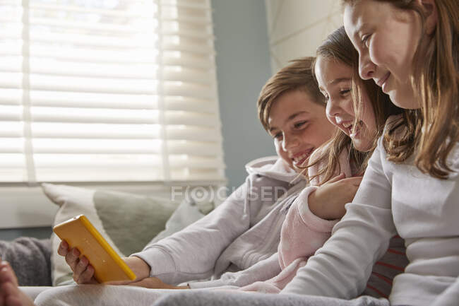 Група дітей сидить на дивані в піжамі, дивлячись на цифрову табличку.. — стокове фото