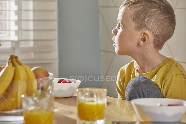 Niño sentado en la mesa del desayuno, mirando por la ventana. - foto de stock