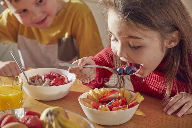 Menino e menina sentados na mesa da cozinha, tomando café da manhã. — Fotografia de Stock