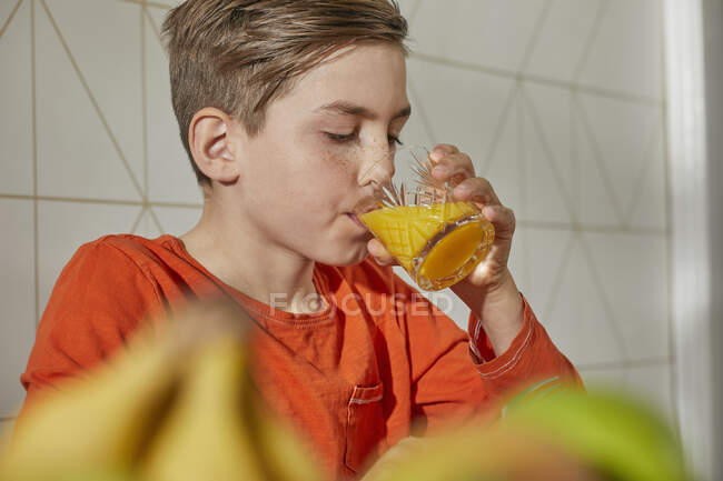 Junge sitzt am Frühstückstisch und trinkt Orangensaft. — Stockfoto