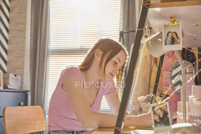 Adolescente sentada em seu quarto em uma mesa, fazendo lição de casa. — Fotografia de Stock