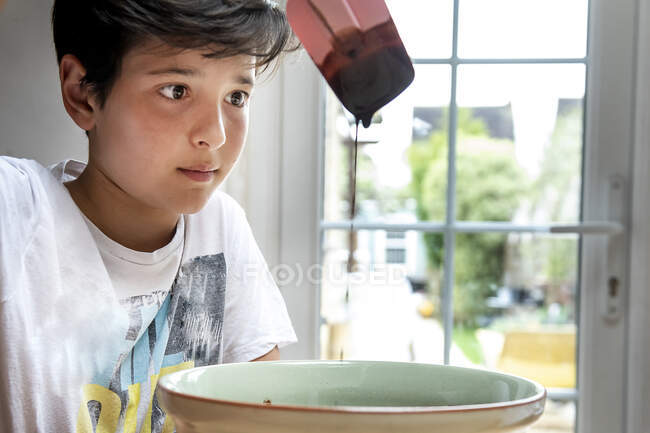 Boy with black hair sitting at a kitchen table, baking chocolate cake. — Stock Photo