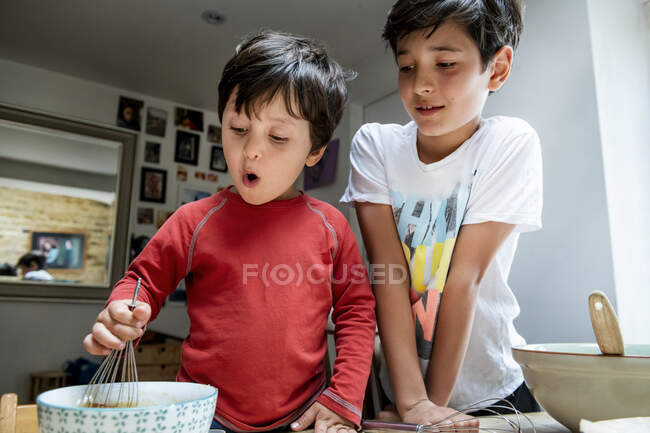 Dos chicos con pelo negro sentados en una mesa de la cocina, horneando pastel de chocolate. - foto de stock