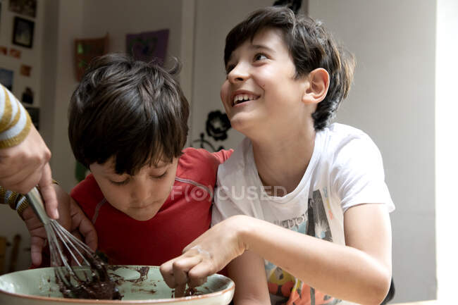 Deux garçons avec les cheveux noirs assis à une table de cuisine, gâteau au chocolat de cuisson. — Photo de stock