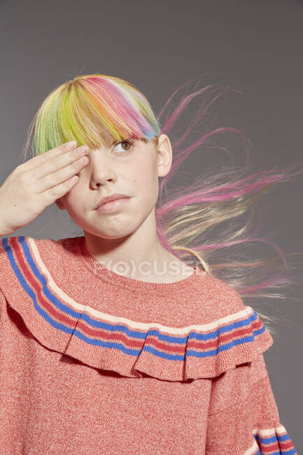 Retrato de niña con el pelo largo y colorido y franja teñida con tapa de volantes de color rosa, mirando hacia otro lado con la mano que cubre el ojo - foto de stock