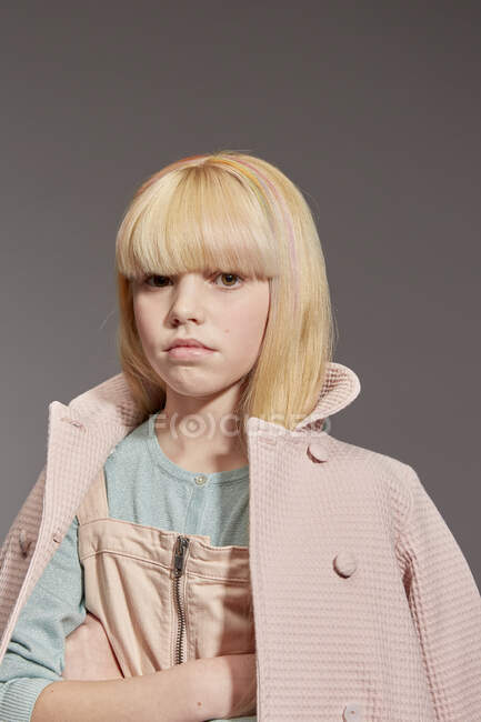 Ernstes Gesicht, Portrait eines Mädchens mit langen blonden Haaren, das einen Mantel trägt, Blick in die Kamera auf grauem Hintergrund — Stockfoto